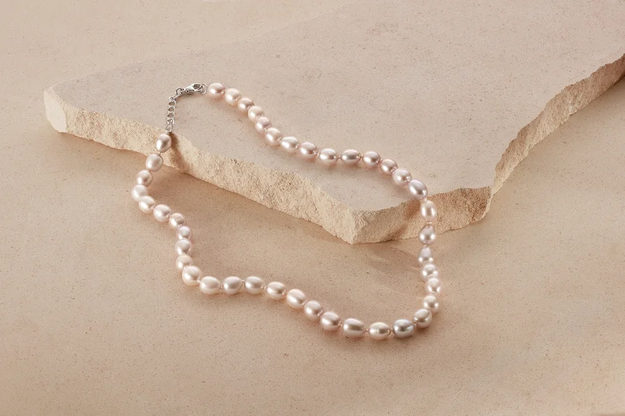 Eine 925 Silber Collier mit Süßwasserzuchtperlen liegt auf beigem Grund.