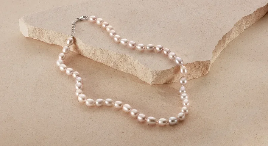 Eine 925 Silber Collier mit Süßwasserzuchtperlen liegt auf beigem Grund.