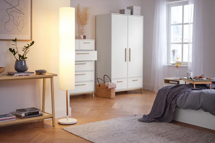 Im Schlafzimmer stehen ein Konsolentisch mit 2 Ablagen, eine Stehleuchte mit Textilschirm, ein Highboard »Eklund« mit Schubladen und ein Kleiderschrank »Eklund« mit Schubladen.