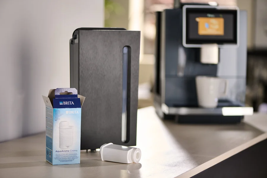 Eine Packung Brita AquaAroma Crema Filter neben einem Filter und einer Kaffeemaschine.