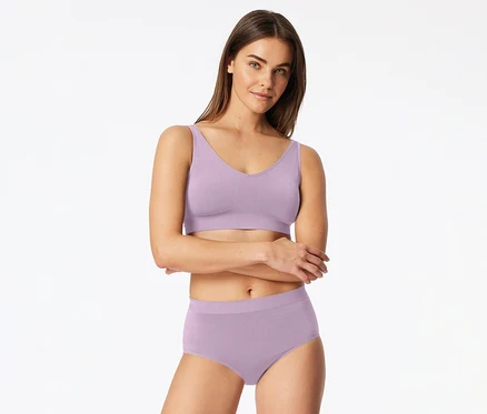 Frau in helllila Bralette und passenden Slips, die Arme verschränkt, blickt nach vorne.