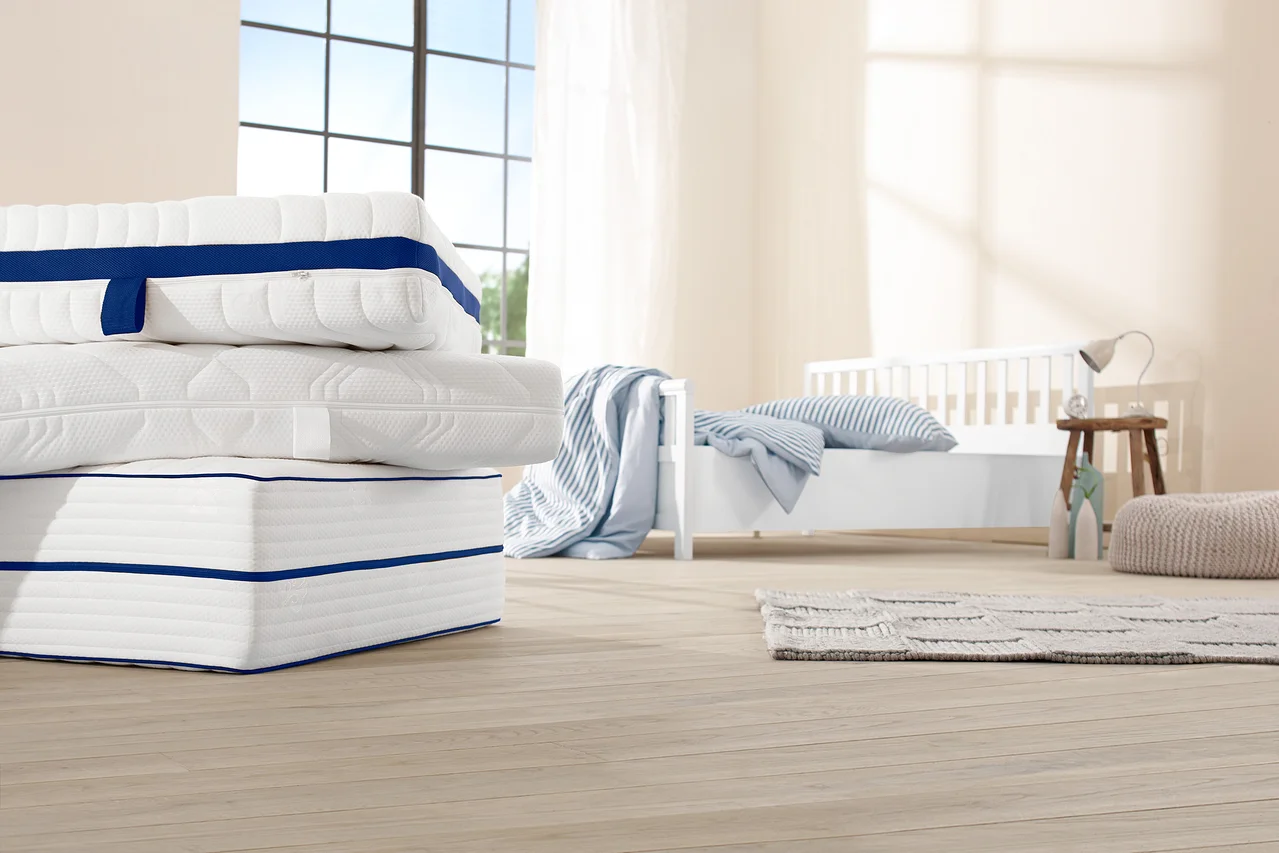 Stapel von weißen 7-Zonen-Tonnentaschenfederkern-Matratzen mit blauen Streifen in einem Schlafzimmer.