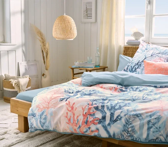 Schlafzimmer mit einem Bett, hellblaues Microfaser-Spannbettlaken in Doppelgröße, Renforcé-Bettwäsche und zwei hellblaue und zwei korallenfarbene Microfaser-Kopfkissenbezüge. Über dem Bett hängt eine Pendelleuchte.