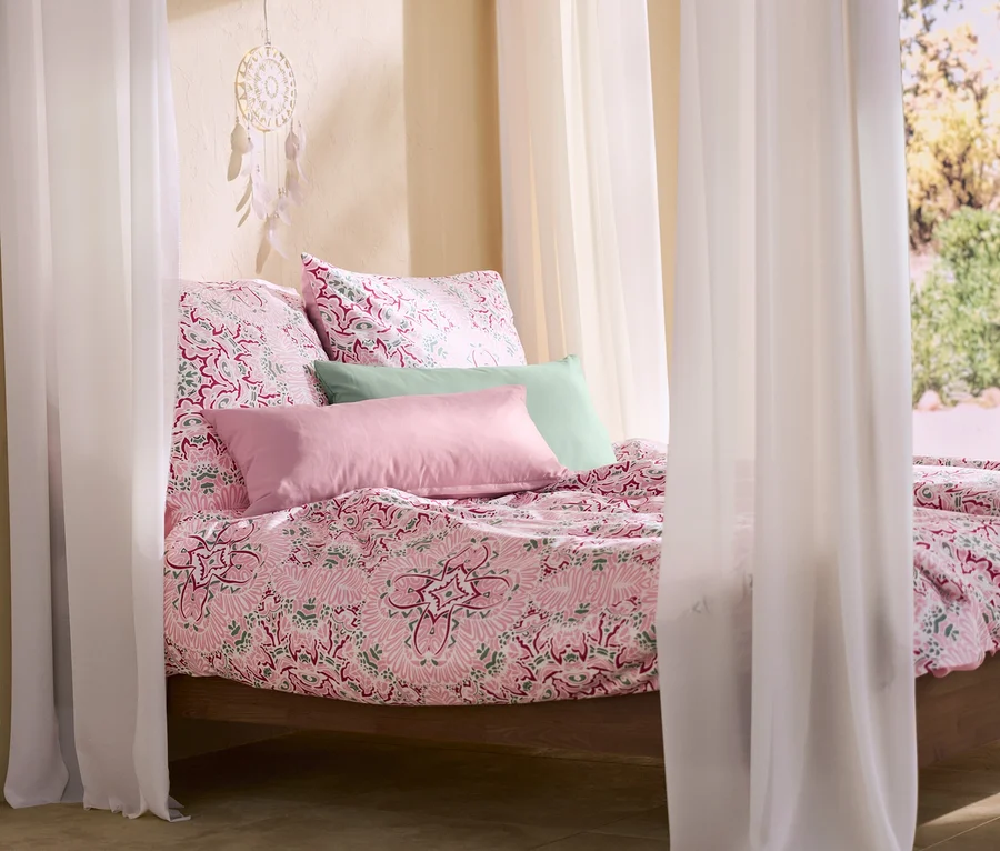 Ein Himmelbett mit rosa Microfaser-Bettwäsche, zwei rosa und zwei grünen Microfaser-Kopfkissenbezügen und einem Traumfänger mit LED-Beleuchtung.