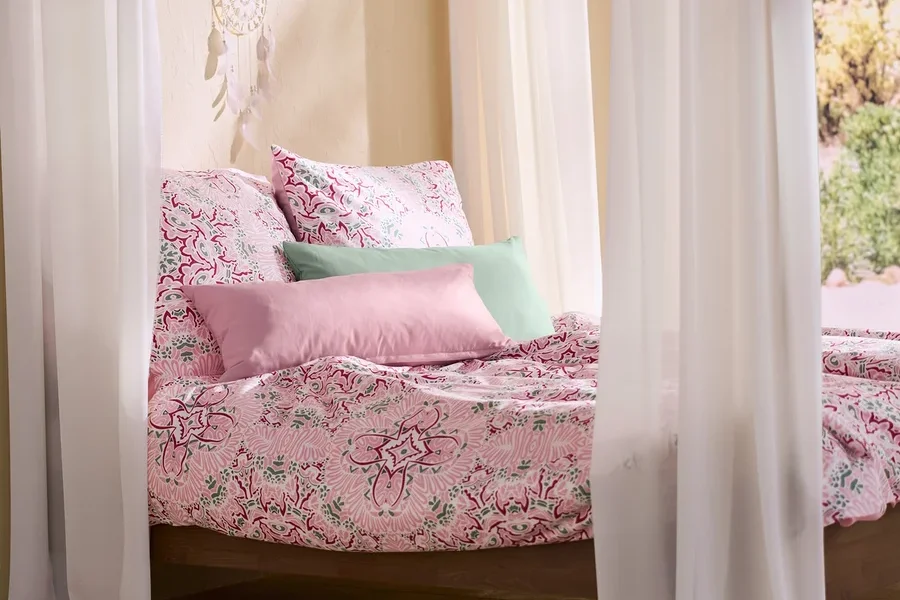 Ein Himmelbett mit rosa Microfaser-Bettwäsche, zwei rosa und zwei grünen Microfaser-Kopfkissenbezügen und einem Traumfänger mit LED-Beleuchtung.