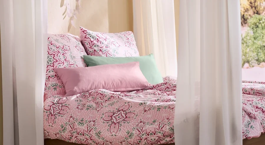 Ein Himmelbett mit rosa Microfaser-Bettwäsche, zwei rosa und zwei grünen Microfaser-Kopfkissenbezügen und einem Traumfänger mit LED-Beleuchtung.