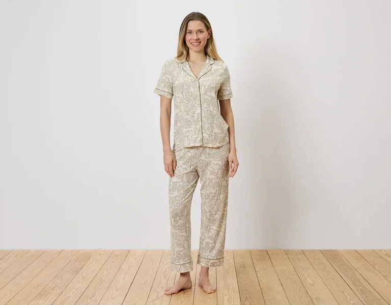 Frau in hell gemustertem Pyjama-Set aus Oberteil mit Knopfleiste und Hose.