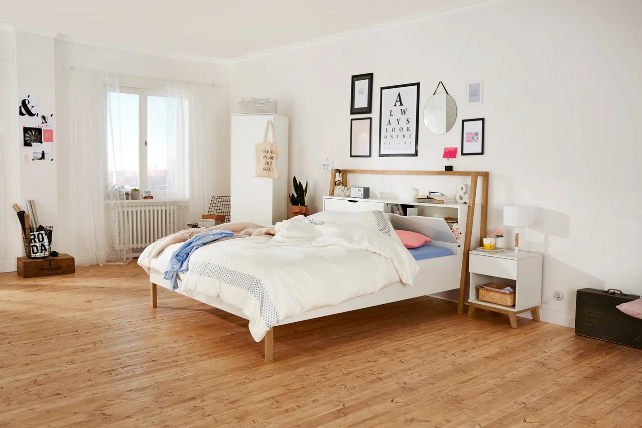 Schlafzimmer mit weißem Bett, Nachttisch und Wanddekorationen.