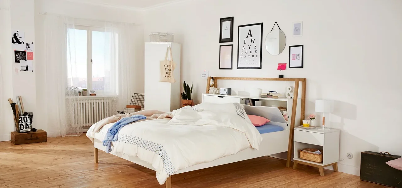 Schlafzimmer mit weißem Bett, Nachttisch und Wanddekorationen.
