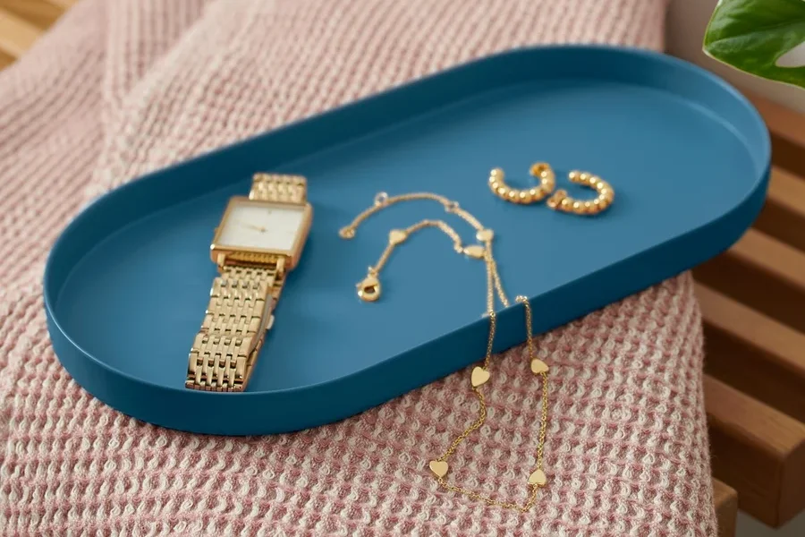 Auf einer Bank liegt ein blaues Tablett aus Metall mit einer Uhr und Schmuck.