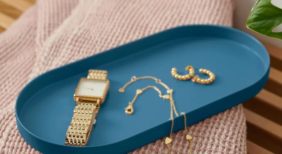 Auf einer Bank liegt ein blaues Tablett aus Metall mit einer Uhr und Schmuck.