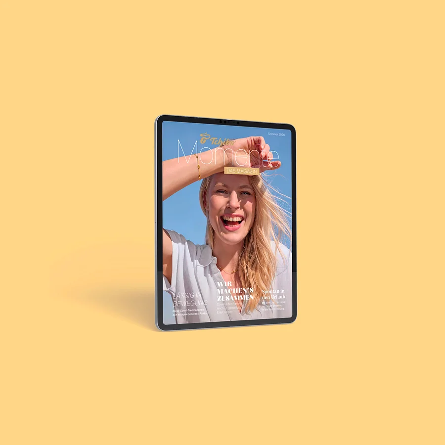 Ein Tablet zeigt das Cover des „Tchibo Momente DAS MAGAZIN“ mit einer lächelnden blonden Frau, die ihre Augen vor blauem Himmel schützt. Texte: „Sommer 2026“, „LÄSSIG IN BEWEGUNG“, „WIR MACHEN'S ZUSAMMEN“, „Spontan in den Urlaub“.