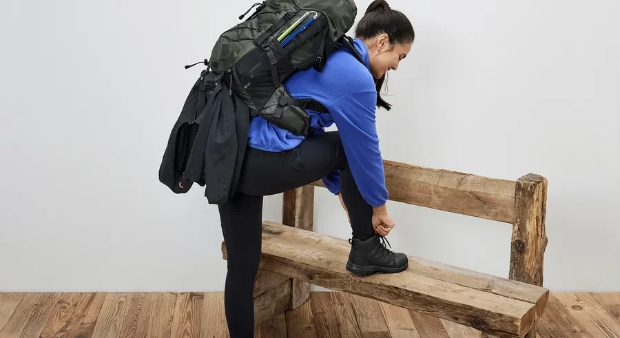 Eine Frau sitzt auf einer Bank und bindet ihre Schuhe. Sie trägt einen 40-l-Wanderrucksack.