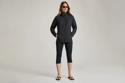 Frau mit Sonnenbrille und schwarzer Softshelljacke. Sie hat die Hände in den Taschen.