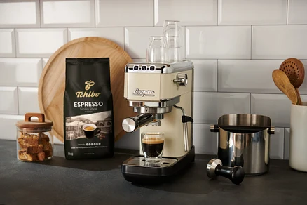 Eine creme »Lapressa« Siebträgermaschine bereitet Espresso in ein Glas zu. Im Hintergrund silberne, rote und schwarze »Lapressa« Siebträgermaschinen und eine Kaffeepackung.