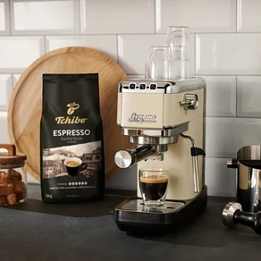 Eine creme »Lapressa« Siebträgermaschine bereitet Espresso in ein Glas zu. Im Hintergrund silberne, rote und schwarze »Lapressa« Siebträgermaschinen und eine Kaffeepackung.