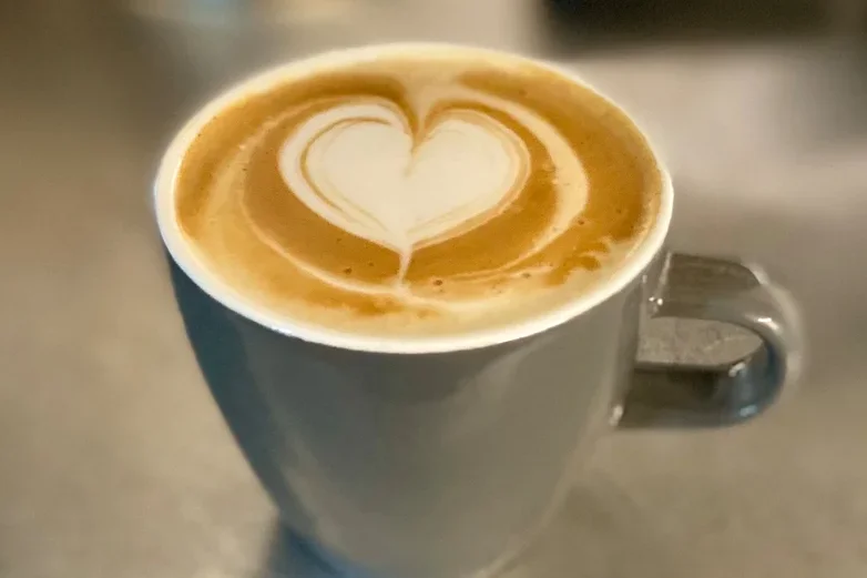 Nahaufnahme einer grauen Tasse mit einem Latte Macchiato, dessen Milchschaum ein Herz formt.
