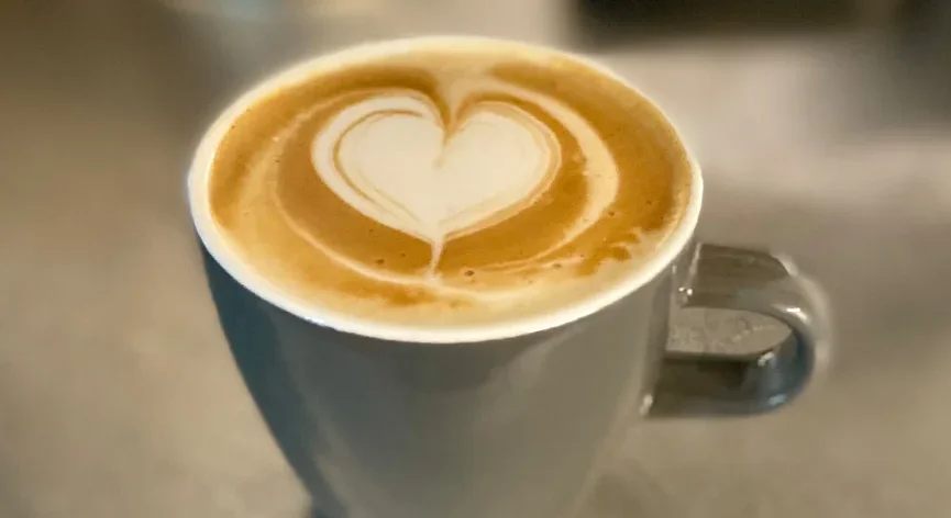 Nahaufnahme einer grauen Tasse mit einem Latte Macchiato, dessen Milchschaum ein Herz formt.