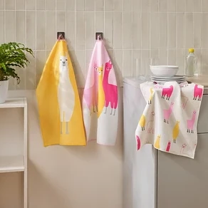Drei Geschirrtücher mit Lama-Motiven hängen in einer Küche neben einem Waschbecken und einem Regal.