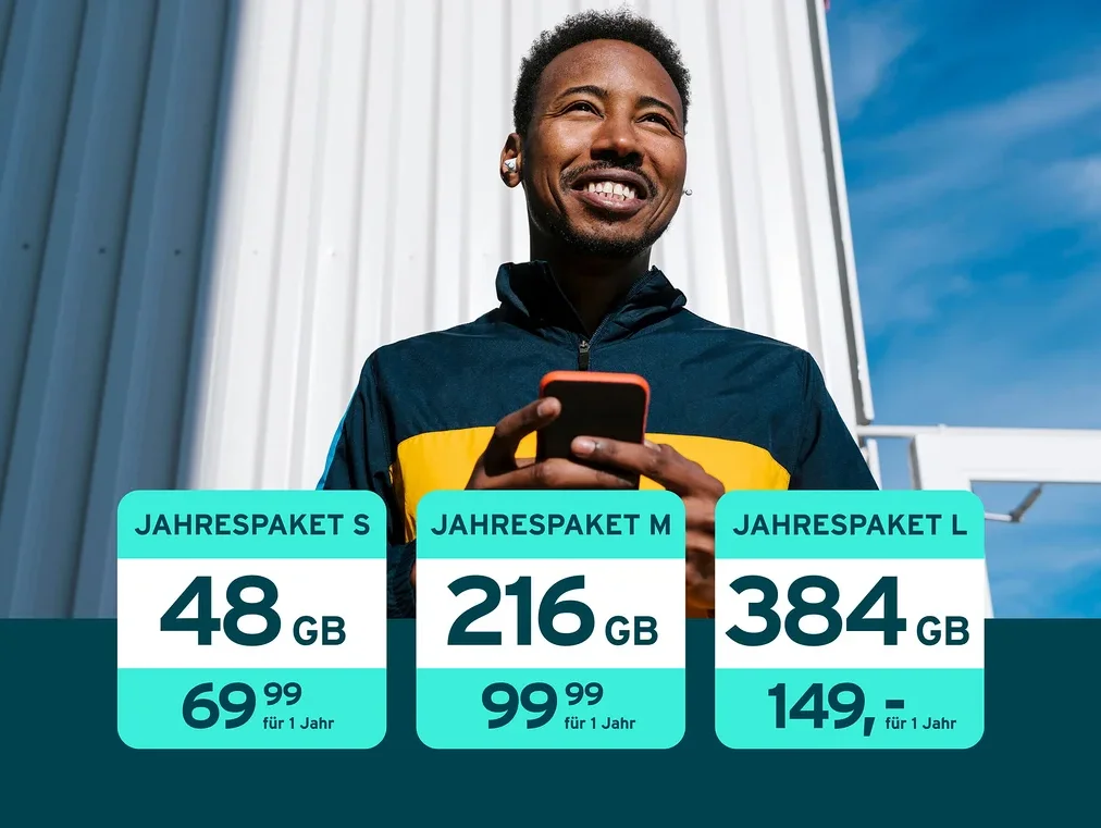 Ein lächelnder Mann mit dunkler Haut, der eine blau-gelbe Jacke und weiße Ohrhörer trägt, blickt nach oben, während er ein rotes Smartphone hält. Drei Datenpaket-Angebote sind überlagert: „JAHRESPAKET S“ mit 48 GB für 69.99, „JAHRESPAKET M“ mit 216 GB für 99.99 und „JAHRESPAKET L“ mit 384 GB für 149,-, alle für 1 Jahr.