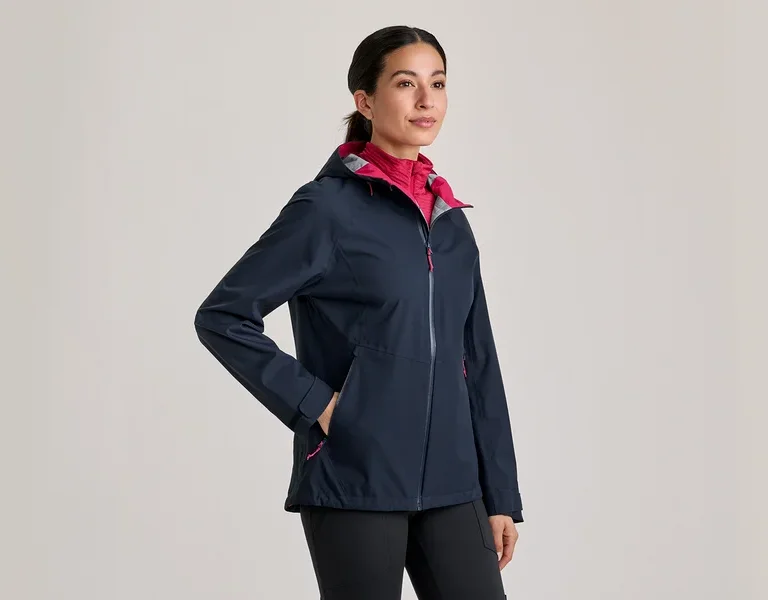 Frau trägt eine dunkelblaue Jacke mit pinkem Innenfutter und schwarzen Hosen, die Hand in der Tasche.