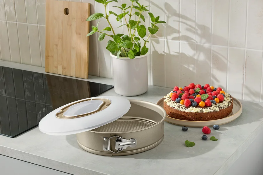 Eine offene Kuchenform mit einem gebackenen Kuchen, der mit Früchten auf einer Küchentheke verziert ist.