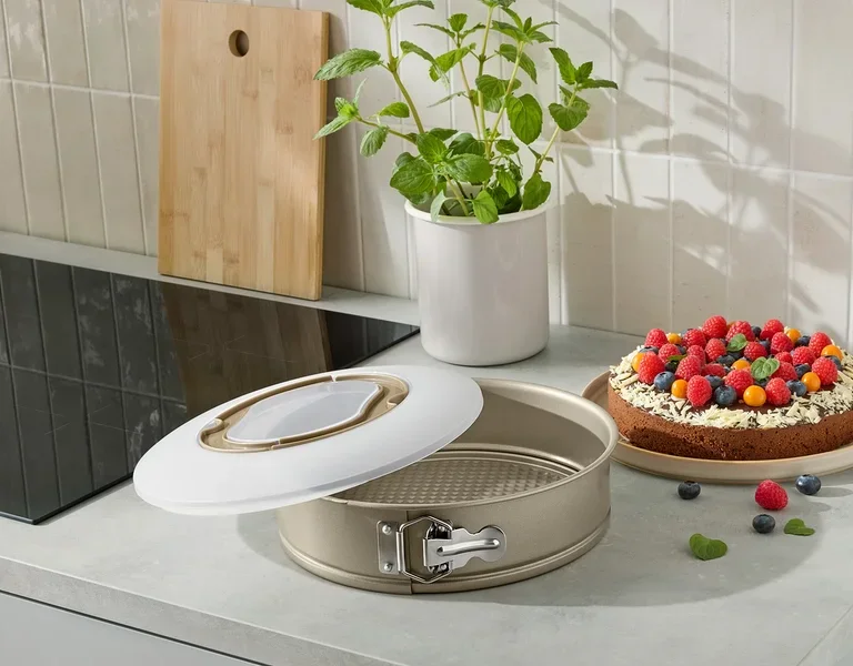 Eine offene Kuchenform mit einem gebackenen Kuchen, der mit Früchten auf einer Küchentheke verziert ist.