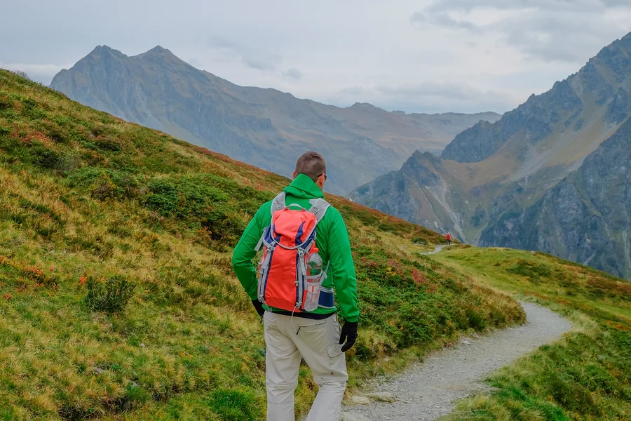 Ein Mann mit einem orangen Rucksack wandert auf einem Pfad in den Bergen.