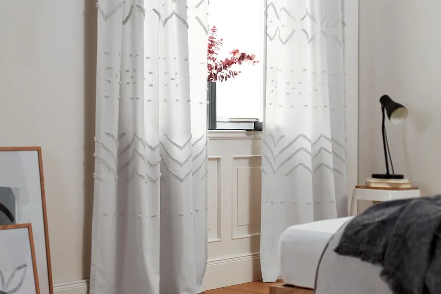 Zwei Vorhangschals mit geometrischen Mustern hängen an einem Fenster.