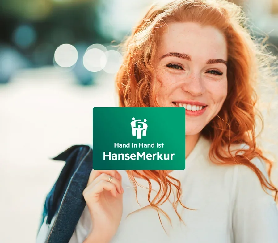 Eine lächelnde rothaarige Frau hält eine grüne Karte mit dem Logo und dem Schriftzug HanseMerkur.