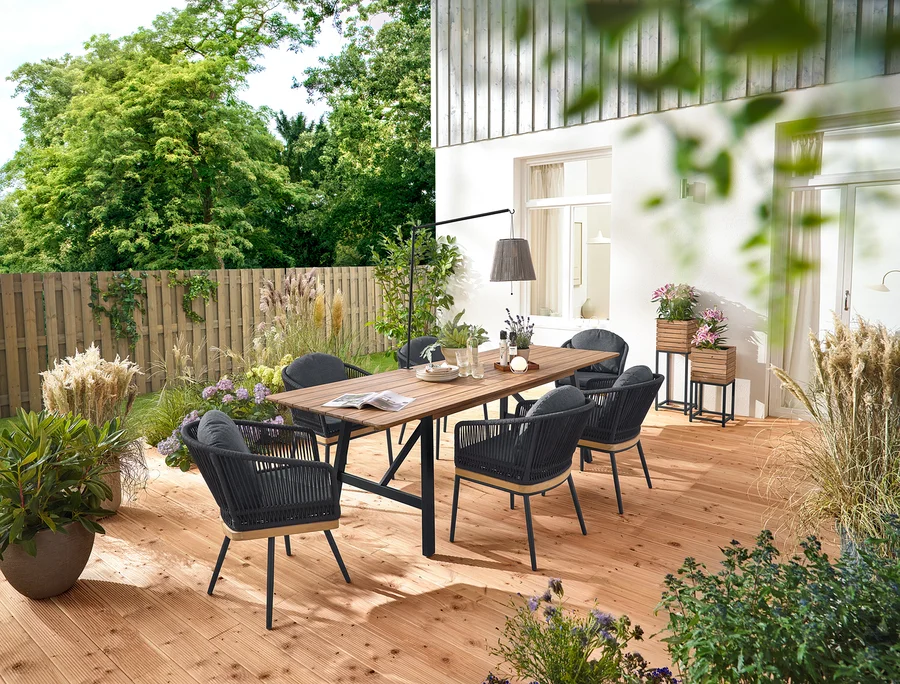 Auf einer Holzterrasse stehen ein ausziehbarer Gartentisch mit rustikalem Gestell, ca. 200-250 cm, drehbare Gartenstühle mit Textilgeflecht und Gartenstühle mit Textilgeflecht. Zwei Pflanzsäulen »Elin« und eine Akku-Solar-Laterne mit Tischhalterung sind ebenfalls zu sehen.