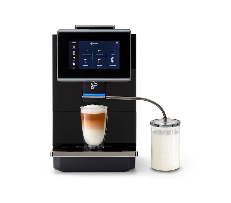 Ein schwarzer Kaffeevollautomat mit Touchscreen bereitet einen Latte Macchiato in einem Glas zu. Ein Milchbehälter ist seitlich angeschlossen.