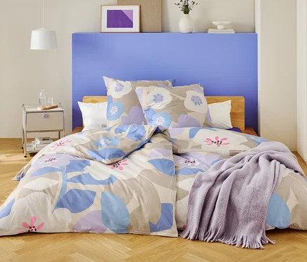 Ein Schlafzimmer mit einem Bett, das mit floraler Bettwäsche und einer lila Decke bedeckt ist.
