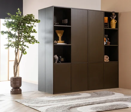 Dunkelbrauner modularer Schrank mit offenen Fächern und geschlossenen Türen, gefüllt mit Dekoartikeln. Links daneben steht eine große Topfpflanze. Davor liegt der WOOOD Teppich »Moro« in Grau und Weiß auf einem hellen Holzboden.
