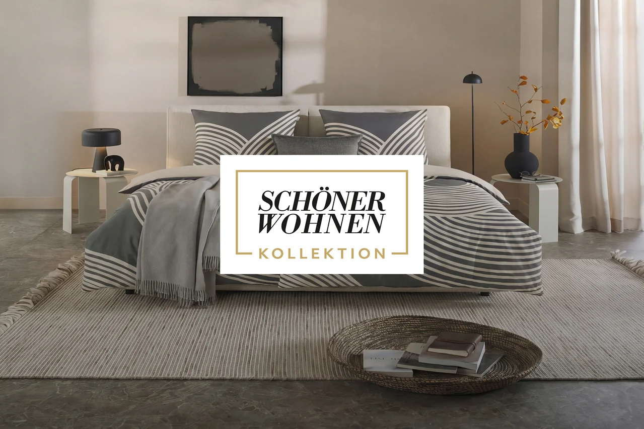 Modernes Schlafzimmer mit einem Bett mit grau-weiß gestreifter Bettwäsche, einem grauen Überwurf, zwei Nachttischen mit Lampen, einem gestreiften Teppich und einem Korb mit Büchern. Über dem Bett hängt ein abstraktes Gemälde.