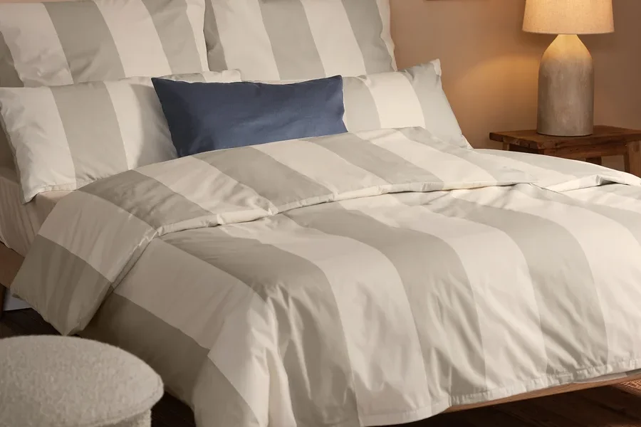 Schlafzimmer-Setup mit beige gestreifter Edelflanell-Bettwäsche, inklusive 2 Kopfkissenbezügen, 2 Dekokissen-Bezüge und Wohndecke.