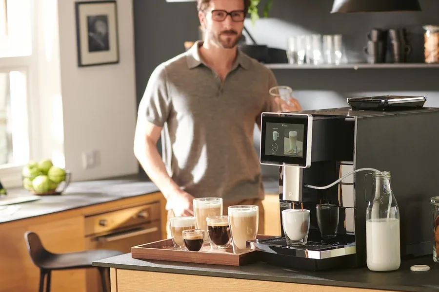 Mann hält Tasse neben »Tchibo Office« Kaffeevollautomat, schwarz.