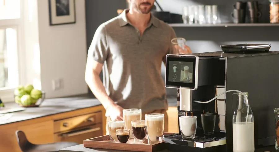 Mann hält Tasse neben »Tchibo Office« Kaffeevollautomat, schwarz.