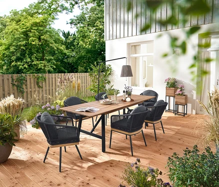 Auf einer Holzterrasse stehen ein ausziehbarer Gartentisch mit rustikalem Gestell, ca. 200-250 cm, drehbare Gartenstühle mit Textilgeflecht und Gartenstühle mit Textilgeflecht. Zwei Pflanzsäulen »Elin« und eine Akku-Solar-Laterne mit Tischhalterung sind ebenfalls zu sehen.