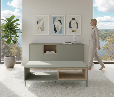 Frau geht an salbeigrünem Sideboard »Hygge« mit 1 Tür vorbei. Darüber hängen drei Bilder. Im Vordergrund steht ein Couchtisch.