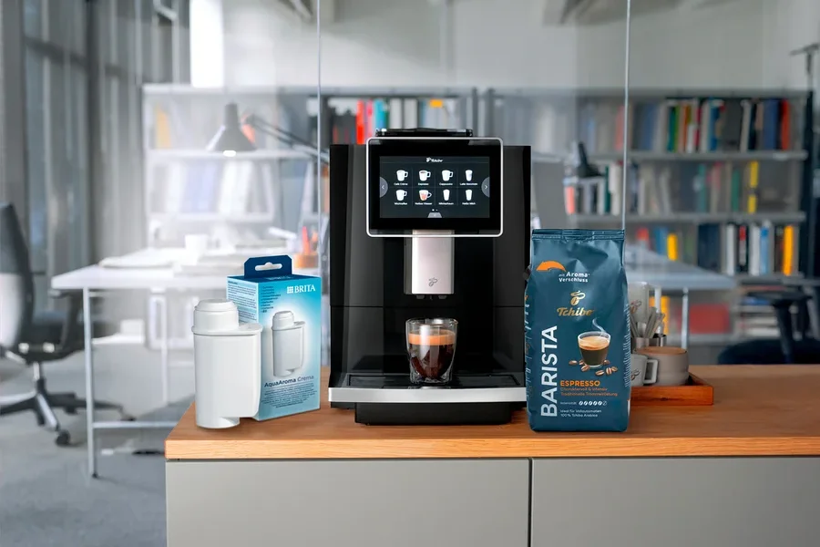 Auf einer Küchentheke stehen eine Kaffeemaschine, eine Packung Brita Wasserfilter und eine Packung Tchibo Barista Espresso.