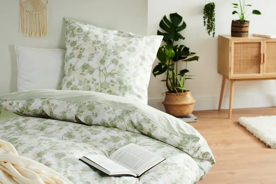 Bett mit blumiger Bettwäsche und offenem Buch. Renforcé-Bettwäsche in Übergröße und Normalgröße sind vorhanden.