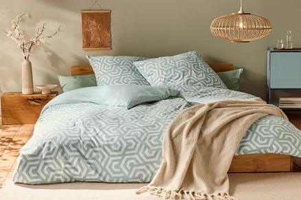 Bett mit Jersey-Bettwäsche, Normalgröße, mit geometrischem Muster und hellgrünen Kissen.