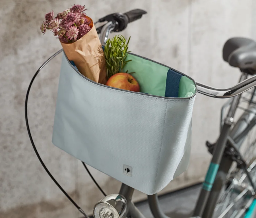 Am Lenker eines Fahrrads befindet sich eine Fahrradlenker-Tasche. In der Tasche befinden sich Blumen, Kräuter und ein Apfel.