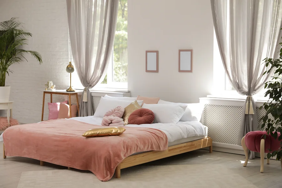 Ein Schlafzimmer mit einem Holzbett, weißen Kissen und einer rosa Tagesdecke.