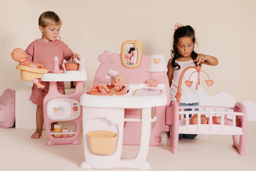 Zwei Kinder spielen mit einem Smoby Baby Nurse Puppen-Spielcenter, das eine Puppenküche, ein Bett und eine Badestation umfasst.