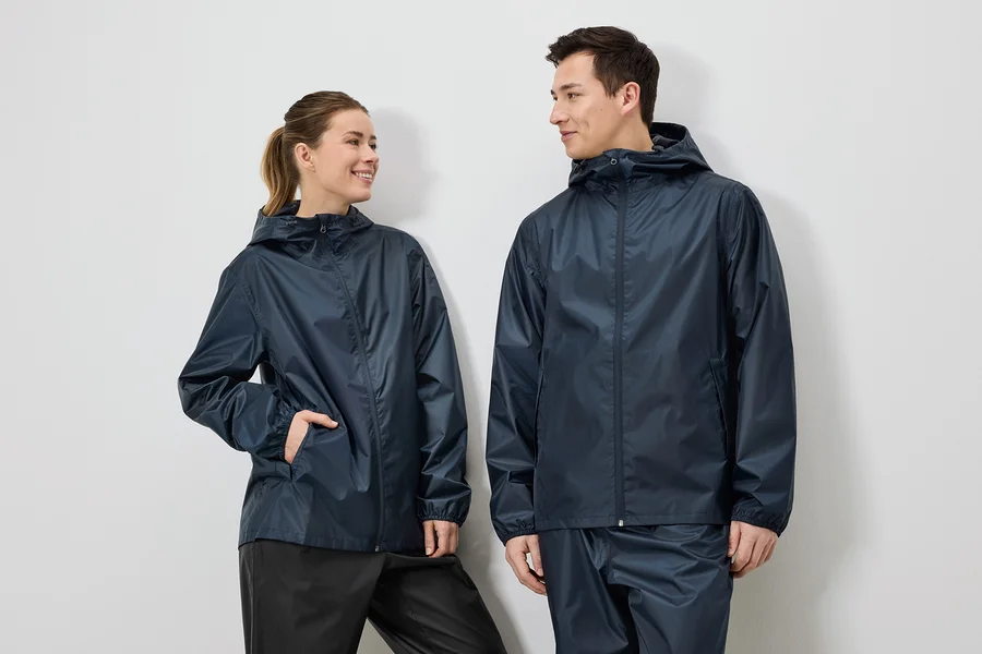 Eine Frau mit Pferdeschwanz und ein Mann tragen marineblaue Regenjacken und Regenhosen vor einem weißen Hintergrund.