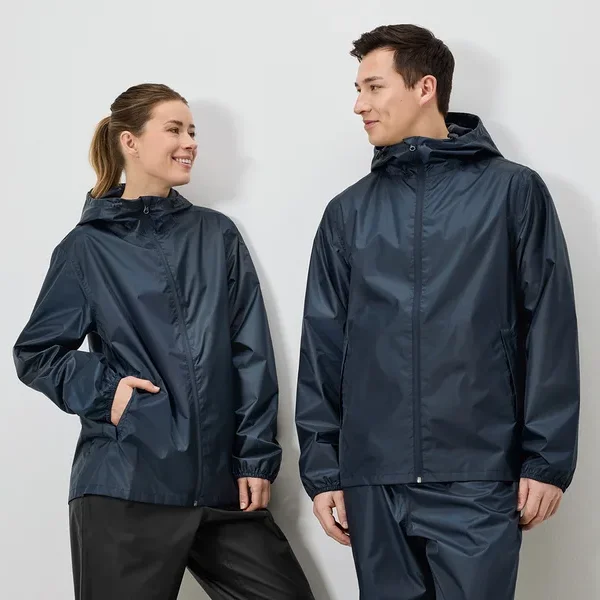 Eine Frau mit Pferdeschwanz und ein Mann tragen marineblaue Regenjacken und Regenhosen vor einem weißen Hintergrund.