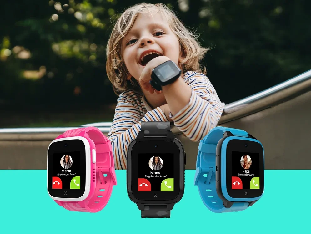 Ein lachendes blondes Kind mit einer schwarzen Smartwatch am Handgelenk lehnt sich im Freien über ein Metallgeländer. Im Vordergrund zeigen drei Smartwatches in Pink, Schwarz und Blau einen eingehenden Anruf an.