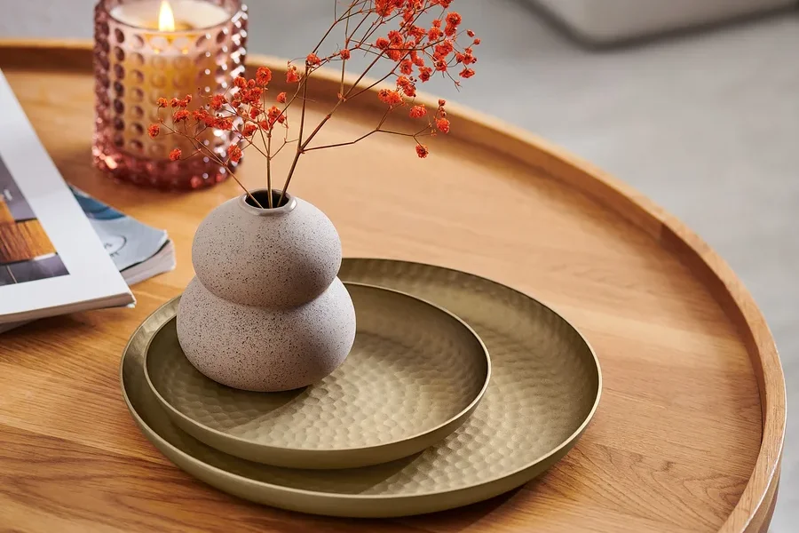 Auf einem Holztisch liegen zwei Dekotabletts, eine Vase mit Blumen und eine Kerze.